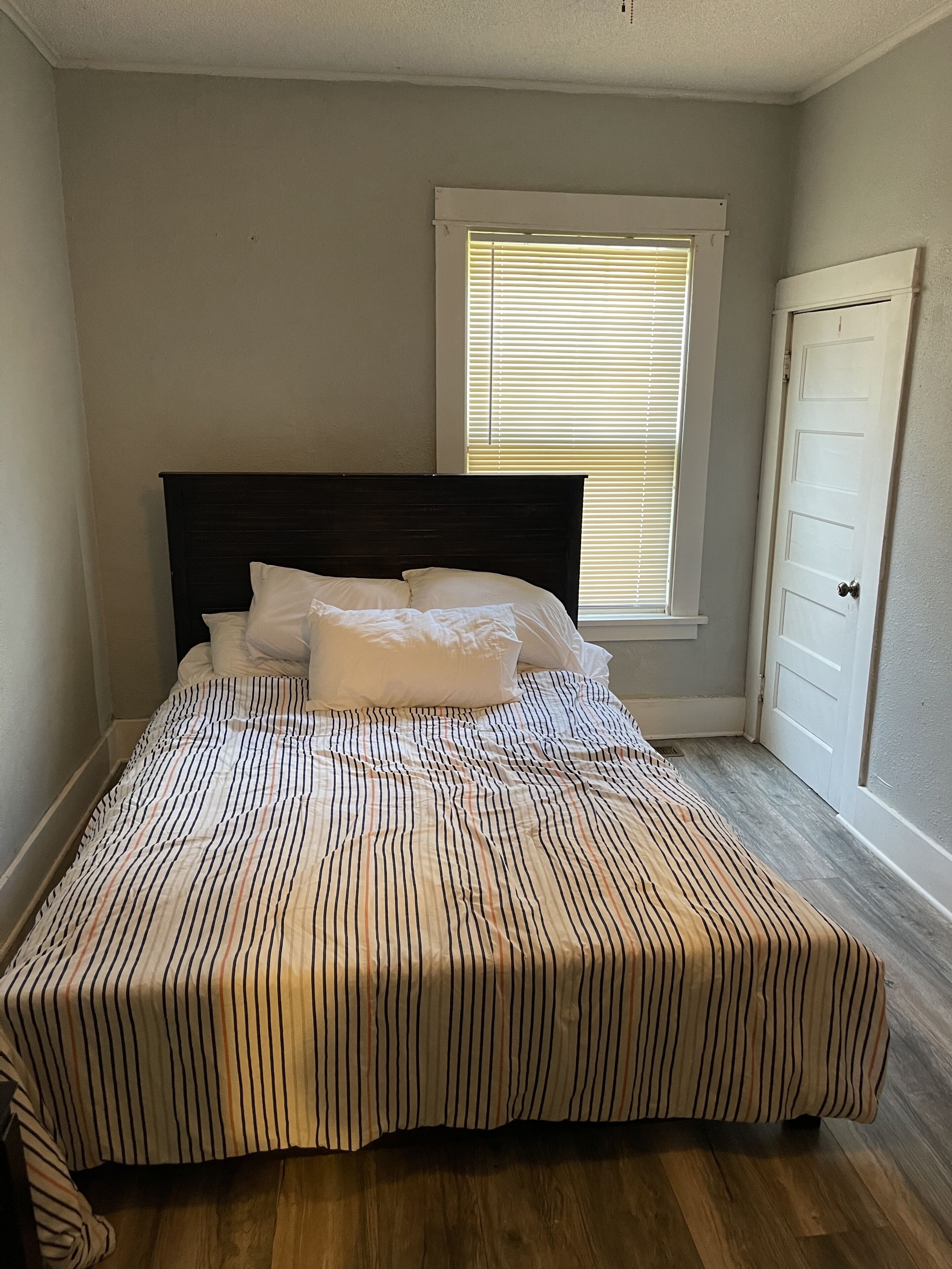 Un dormitorio con cama, ventana con persianas y puerta.