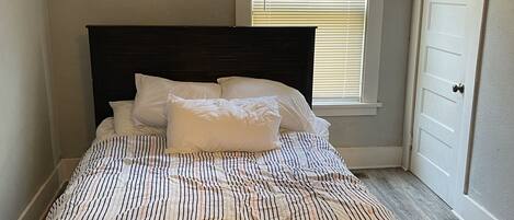 Un dormitorio con cama, ventana con persianas y puerta.