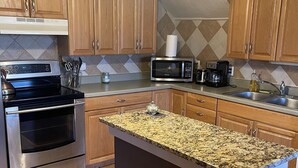 A kitchen with wooden cabinets, a granite countertop island, stainless steel appliances, and a chandelier. - Downtown Des Moines (Des Moines)