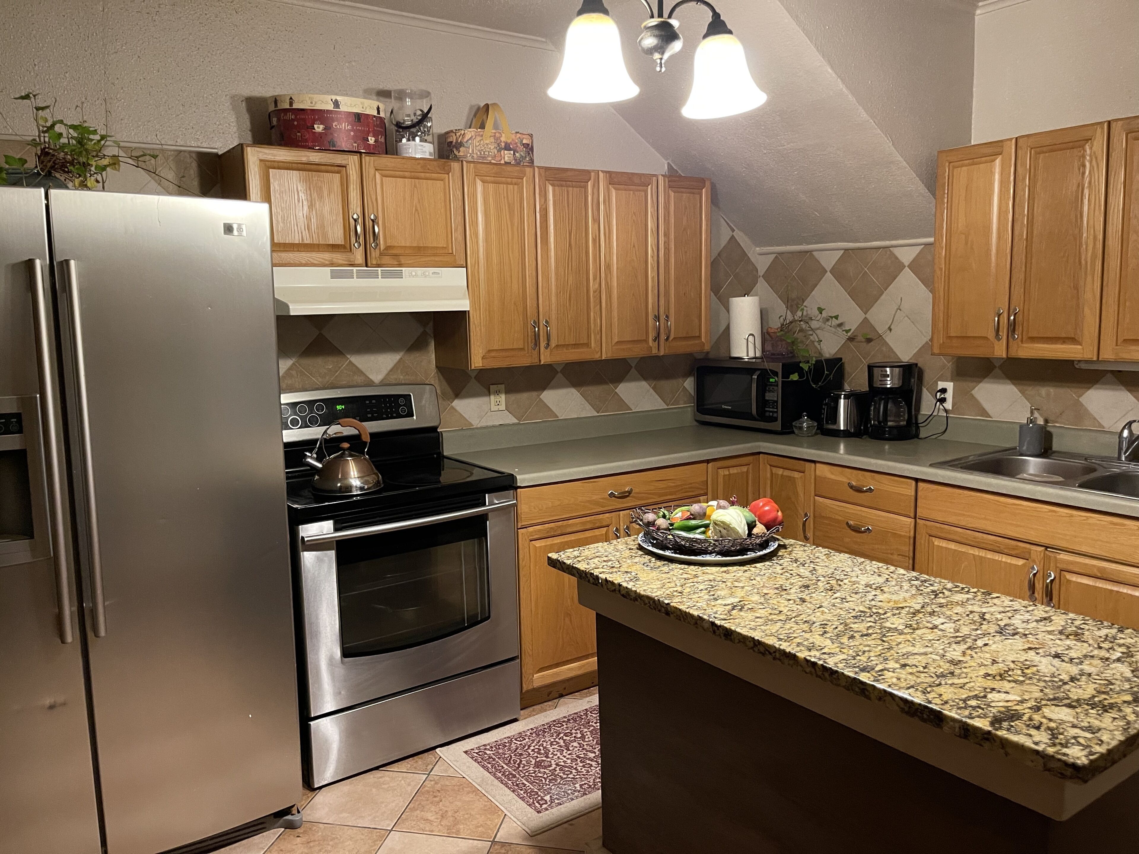 Una cocina con armarios de madera, electrodomésticos de acero inoxidable, una encimera de granito y una pequeña isla.