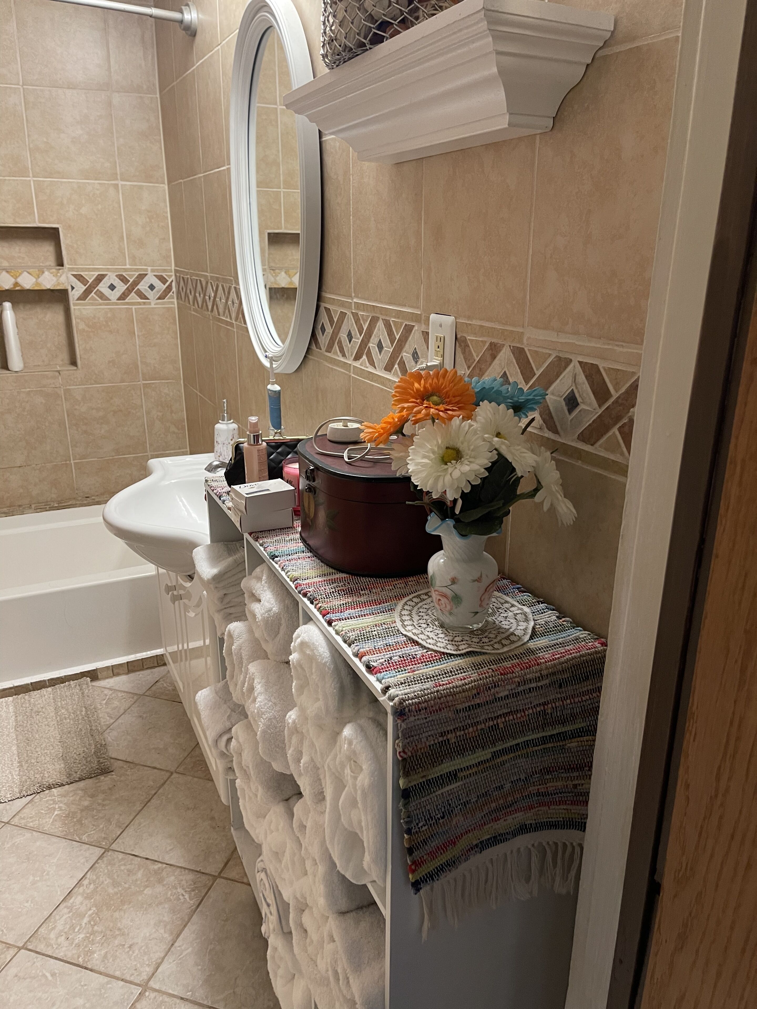 A bathroom with a white sink, a mirror, a towel rack, and a decorative vase with flowers.