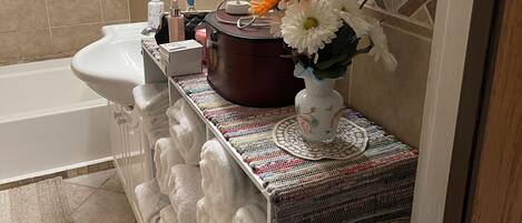 A bathroom with a white sink, a mirror, a towel rack, and a decorative vase with flowers.