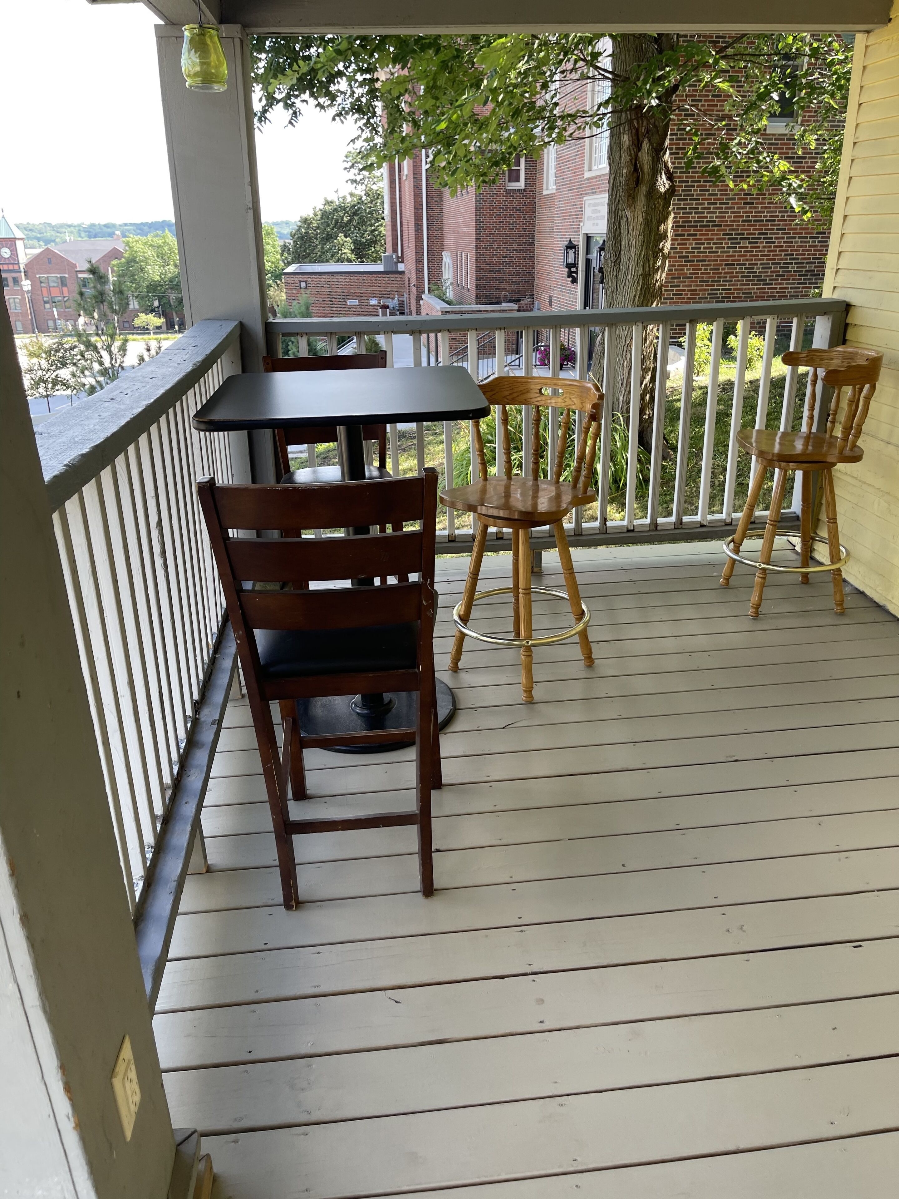 A wooden deck with a table and chairs, a hanging light fixture, and a view of buildings in the background.