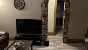 A living room with a stone archway, a flat-screen TV, a coffee table with decorative items, and a patterned rug. - Downtown Des Moines (Des Moines)
