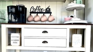 En köksbänk med en kaffetematisk dekoration, inklusive ett hyllsystem för kaffemuggar och en skylt med texten ”Kaffe är alltid en bra idé”.
