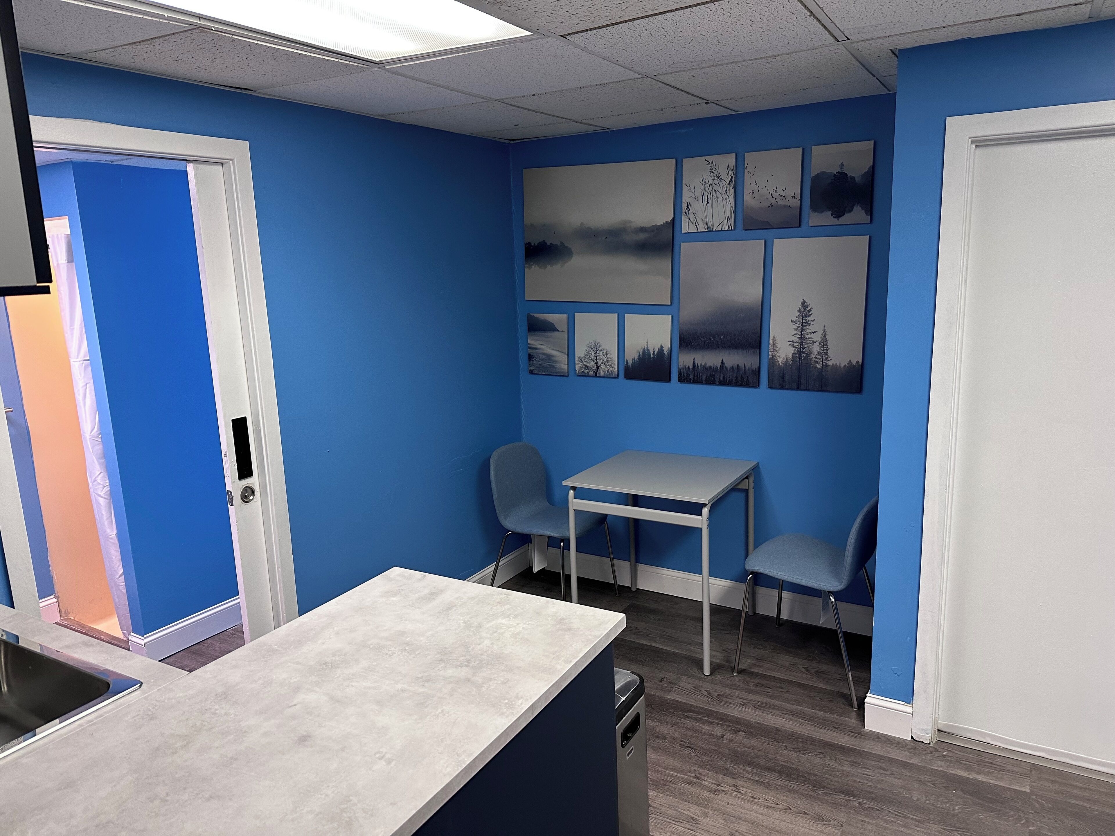 A room with blue walls, a white door, a small table with two chairs, and a window with blinds.