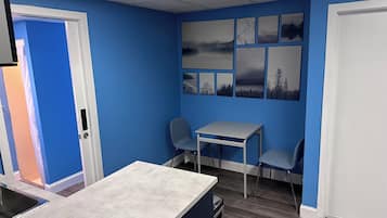 A room with blue walls, a white door, a small table with two chairs, and a window with blinds.