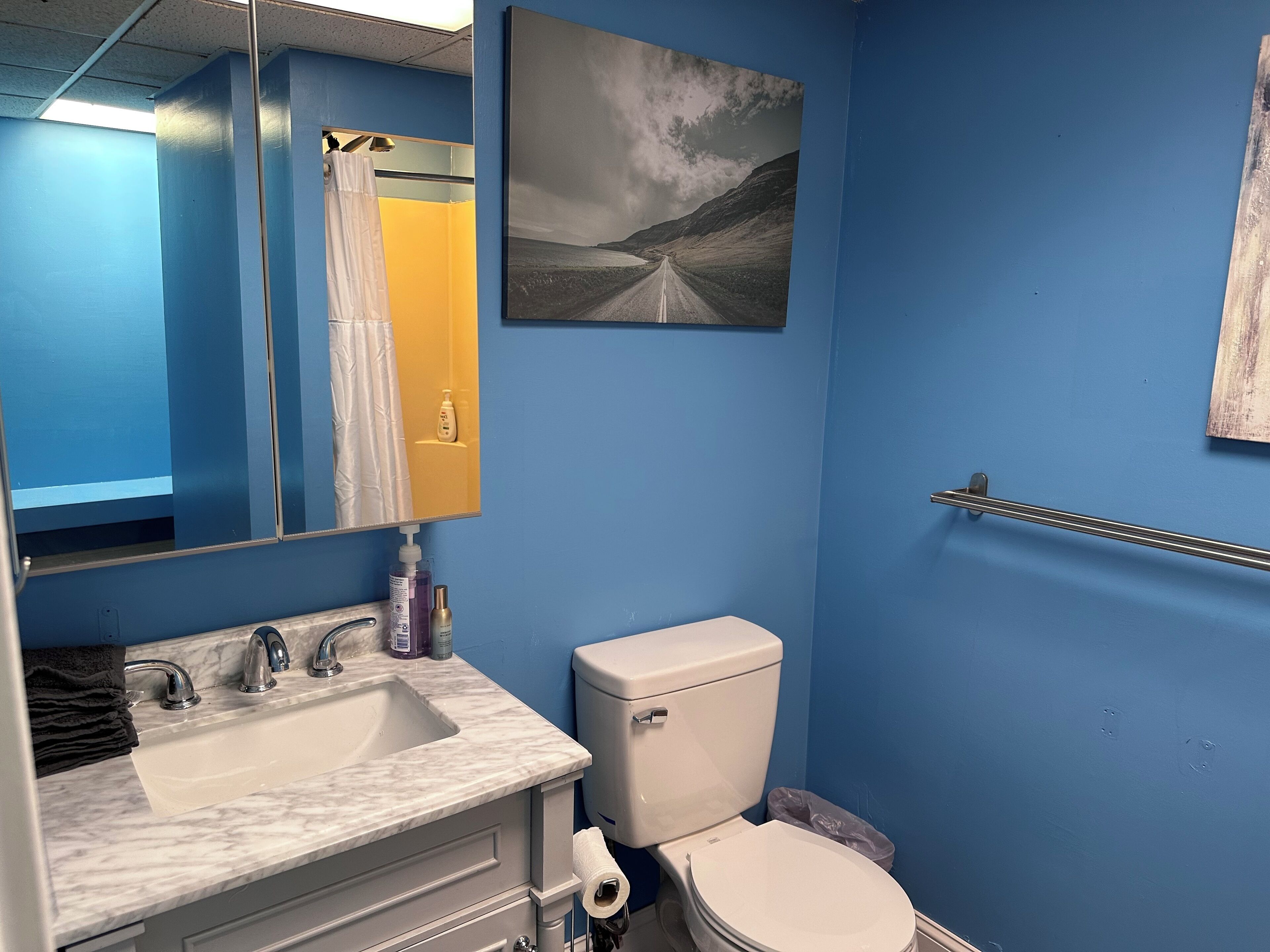 A bathroom with a sink, mirror, toilet, and a towel rack.