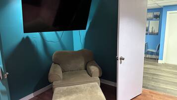 Ein Zimmer mit türkisfarbenen Wänden, einem beigen Sessel, einem an der Wand montierten Flachbildfernseher und einer weißen Tür.