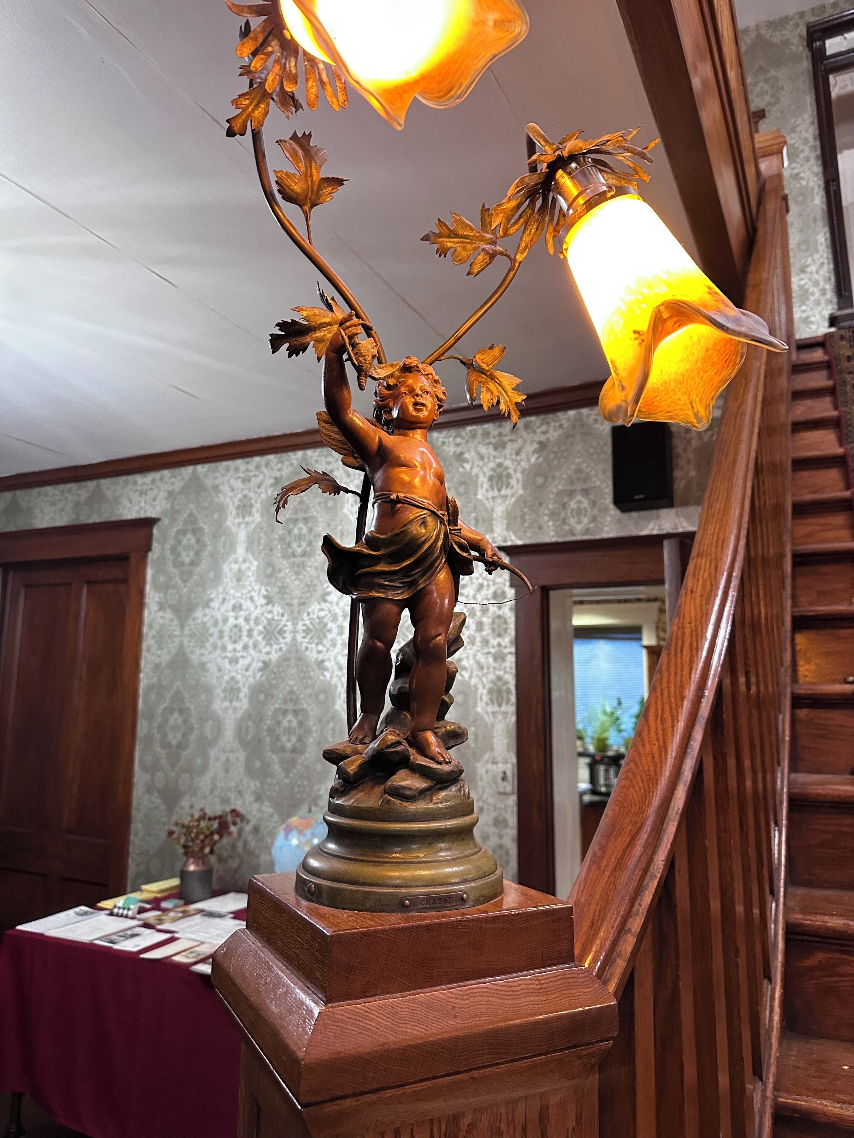 A wooden statue of a cherub with a bow and arrows, mounted on a pedestal with a brass plaque reading "CHASE".