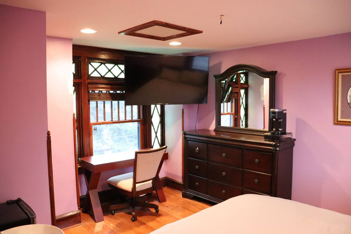 Une chambre à coucher comprenant un lit, un bureau, une chaise, une commode et un téléviseur fixé au mur.