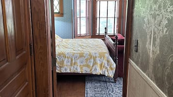 A narrow hallway leading to a bedroom with a bed, a dresser, and a window with shutters.
