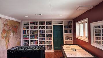 A room with a foosball table, a pool table, and bookshelves filled with books.