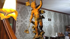 Eine Statue einer Figur, die eine Blume und eine Schaufel hält, auf einem hölzernen Sockel mit einer Beschriftung.