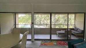 Ein geräumiges Wohnzimmer mit einem großen Schiebeglasfenster, das auf einen Balkon führt, einem Esstisch mit Stühlen und einem Sofa.