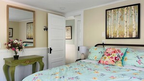 Una camera da letto con una coperta a fiori, un tavolino verde con un vaso di fiori, uno specchio grande e un quadro appeso al muro.