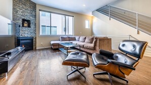A modern living room with a stone fireplace, a large window, a sofa, and a staircase. - Post-Worthy Rooftop Views / Super Walkable LoHi Area / Modern 3b3b (Denver)