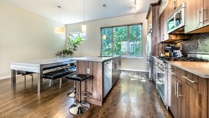 A modern kitchen with a central island, bar stools, stainless steel appliances, and a view of greenery outside. - Post-Worthy Rooftop Views / Super Walkable LoHi Area / Modern 3b3b (Denver)