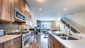 A modern kitchen with wooden cabinets, stainless steel appliances, and a large island with a sink. - Post-Worthy Rooftop Views / Super Walkable LoHi Area / Modern 3b3b (Denver)