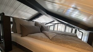 A bedroom with a sloped ceiling, a bed with multiple pillows, and a wooden floor.