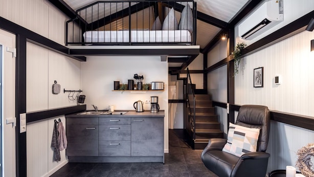 A modern kitchen with a central island, a staircase leading to an upper level, and a seating area with a leather chair and a side table.