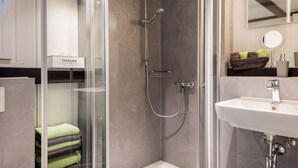 A modern bathroom with a glass-enclosed shower, a white sink, and a towel rack with green and brown towels.