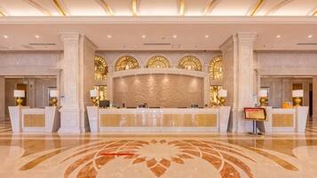 Zona de recepción de un hotel con piso de mármol, un mostrador central y arcos decorativos.