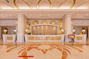 Zona de recepción de un hotel con piso de mármol, un mostrador central y arcos decorativos.