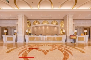 Zona de recepción de un hotel con piso de mármol, un mostrador central y arcos decorativos.