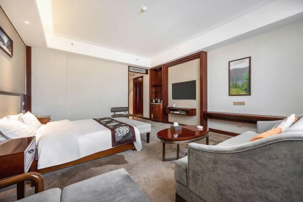 Una habitación de hotel con cama, sofá, escritorio, televisor y espejo.