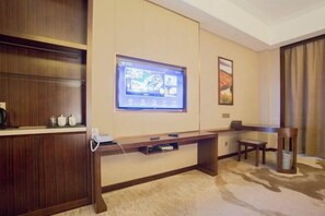 Habitación de hotel con un escritorio de madera, un televisor de pantalla plana montado en la pared, una mesita pequeña y un cubo de basura.