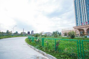 A curved pathway with a green metal fence, a building with a beige facade, and a tall blue structure in the background. - Jinze Ali Mali Hotel (Khorgas)