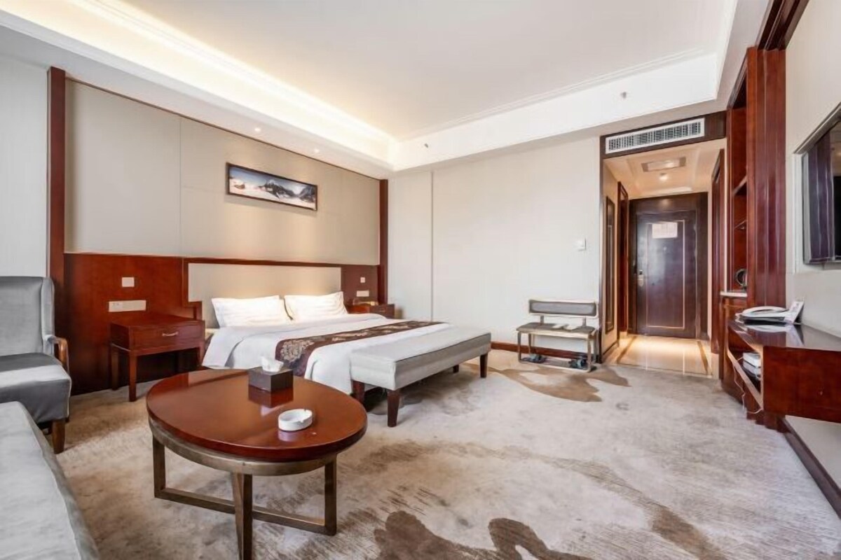Habitación de hotel con cama, escritorio, silla, mesa redonda y perchero.