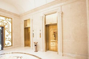 A lobby with three elevators, a marble floor, and a decorative wall panel.