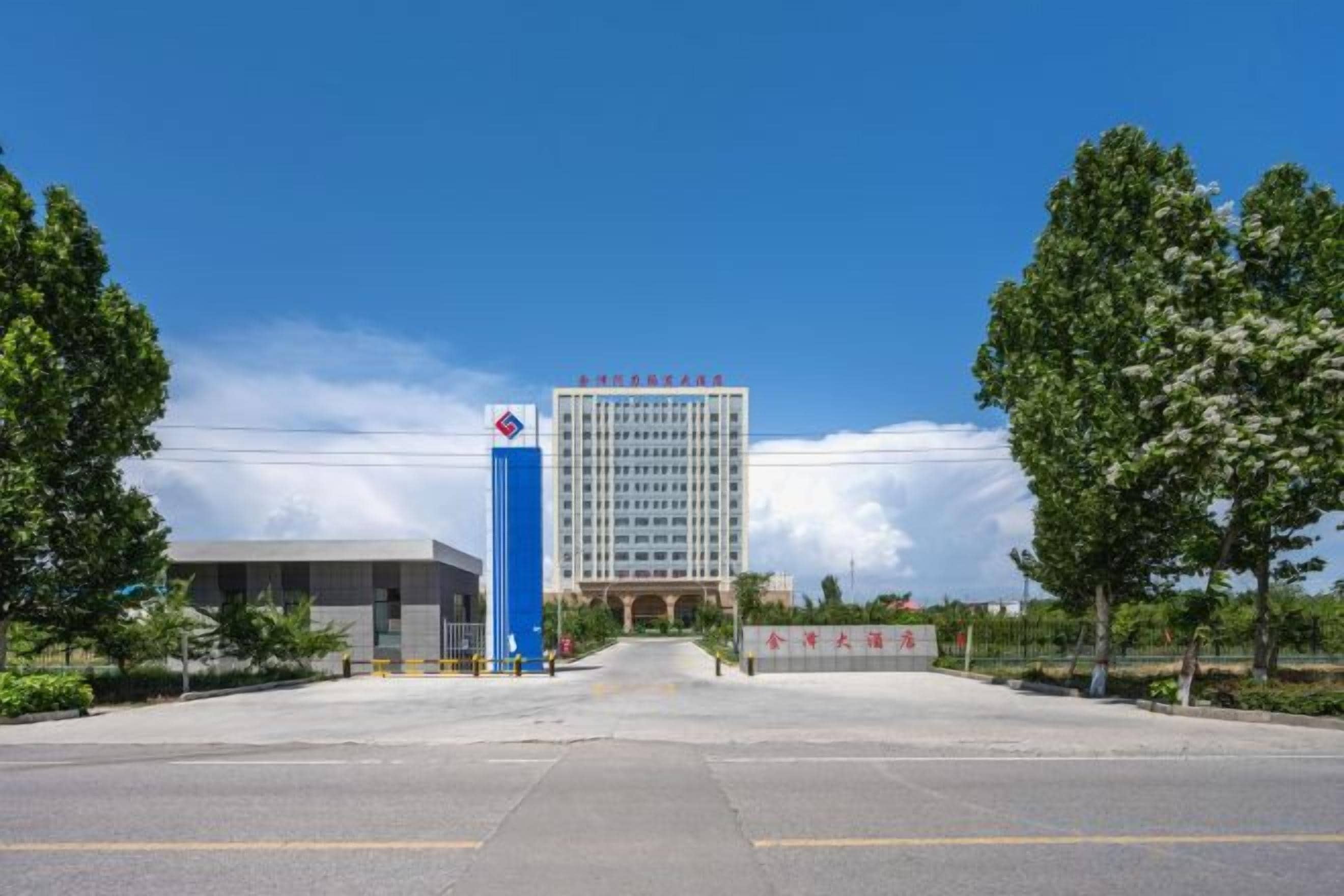 A building with a prominent blue and white sign, a clear sky, and trees in the foreground.