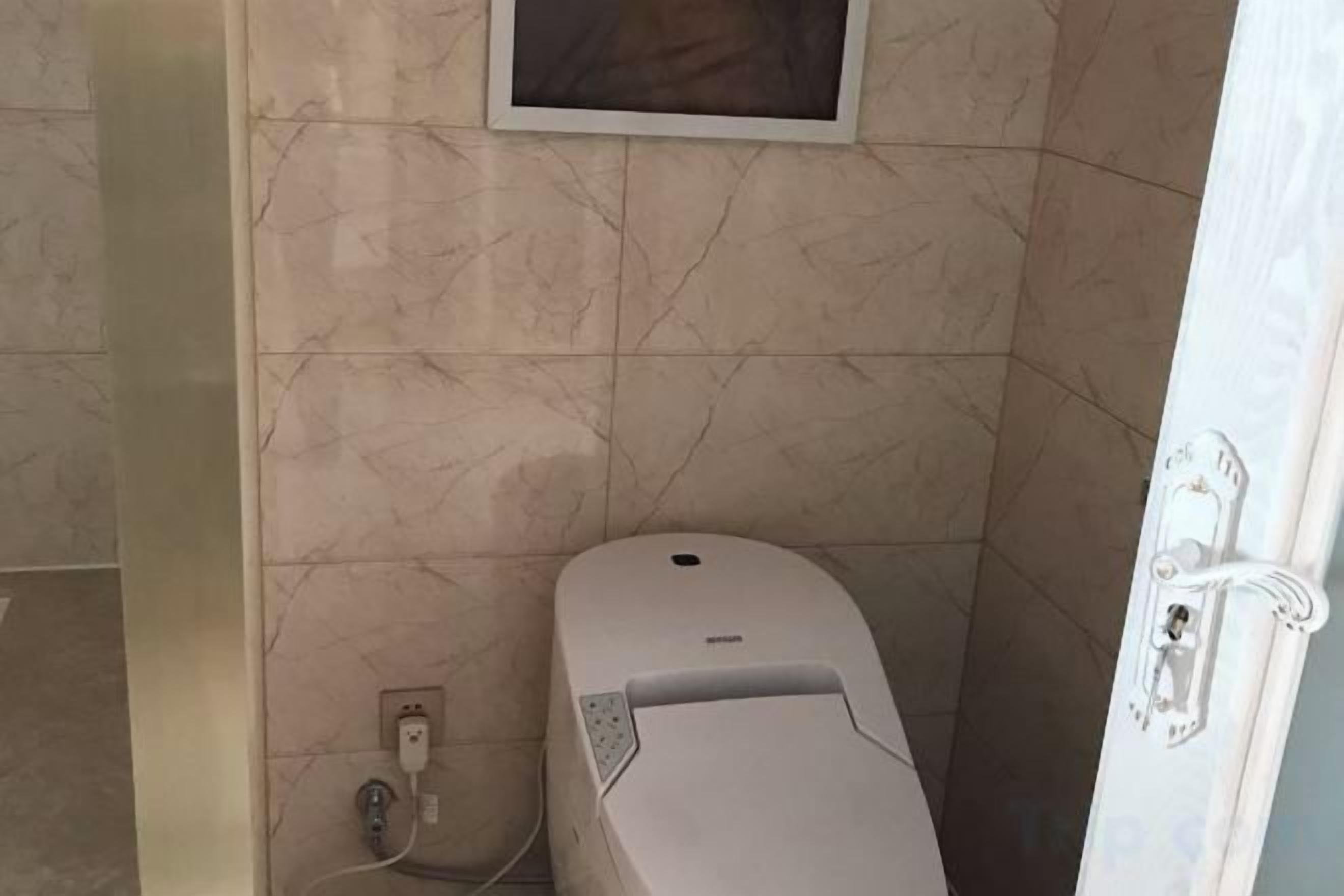 Un bany amb vàter, una presa elèctrica a la paret i una porta amb màneig.
