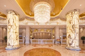 Un hall dâentrĂ©e ornĂ© de colonnes en marbre, dotĂ© dâun grand lustre et dâun comptoir dâaccueil.