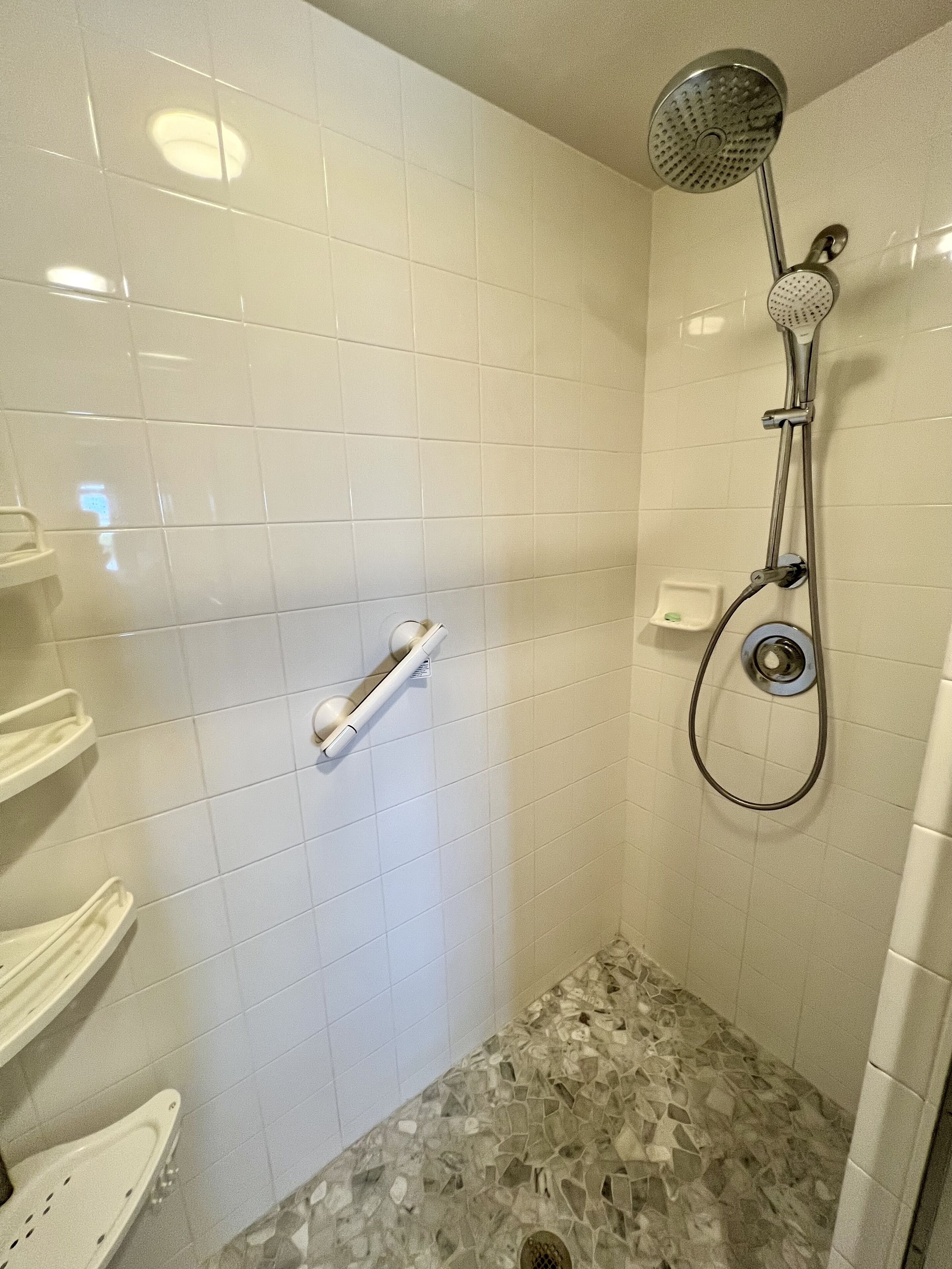 A shower with a handheld showerhead and a wall-mounted faucet.