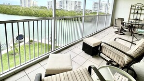 En balkon med udsigt over vand og bygninger, møbleret med en sofa, stole og et bord.