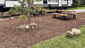 A recreational vehicle (RV) with a "SPORTSMEN" decal, a picnic table, and a small tree in the foreground. - The Hideaway at Glacier Meadows - Luxury Camper (Martin City)