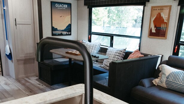 A modern kitchen with a built-in sink, a wooden utensil holder, and a view of a living area with a couch and a poster on the wall. - The Hideaway at Glacier Meadows - Luxury Camper (Martin City)