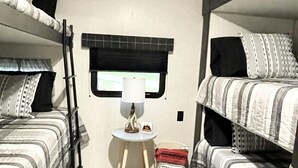 A compact room with bunk beds, a small table with a lamp, and a window with a view. - The Hideaway at Glacier Meadows - Luxury Camper (Martin City)
