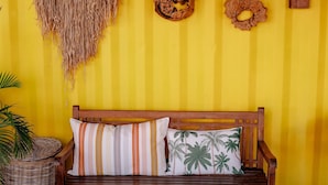 A wooden bench with striped and palm tree patterned cushions against a yellow wall with vertical stripes. - TIPI 2 Kalbas • Domaine de Meilly (Saint-Louis)