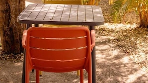 A table and chairs set outdoors with a tree and plants nearby. - TIPI 2 Kalbas • Domaine de Meilly (Saint-Louis)