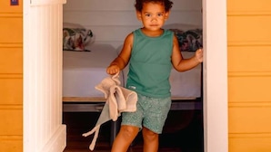 A child in a green sleeveless top and patterned shorts standing in a doorway with a wooden sign above reading "KANPECH". - TIPI 2 Kalbas • Domaine de Meilly (Saint-Louis)