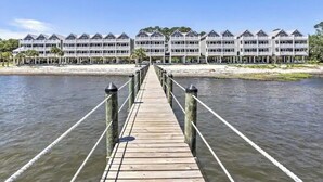 Une jetée en bois mène à un hôtel en bord de mer, doté de nombreux balcons et offrant une vue dégagée sur l’océan.