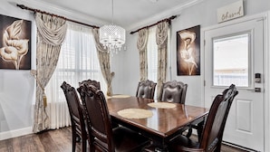 Un comedor con una mesa de madera, seis sillas y cortinas decorativas.