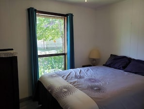 Een slaapkamer met een bed, nachtkastje, lamp en een raam met gordijnen.