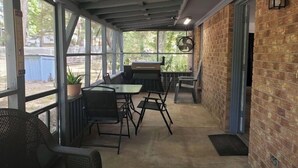 Un patio couvert avec une table et des chaises, un barbecue et une vue sur l’extérieur.