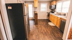A kitchen with wooden flooring, a black refrigerator, wooden cabinets, a microwave, and a sink.